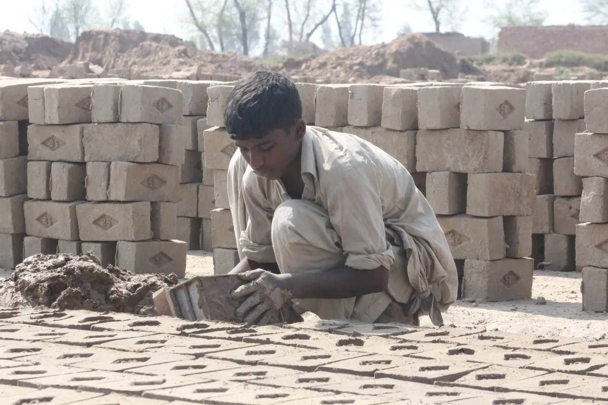A young boy shaping bricks by hand at a brick kiln